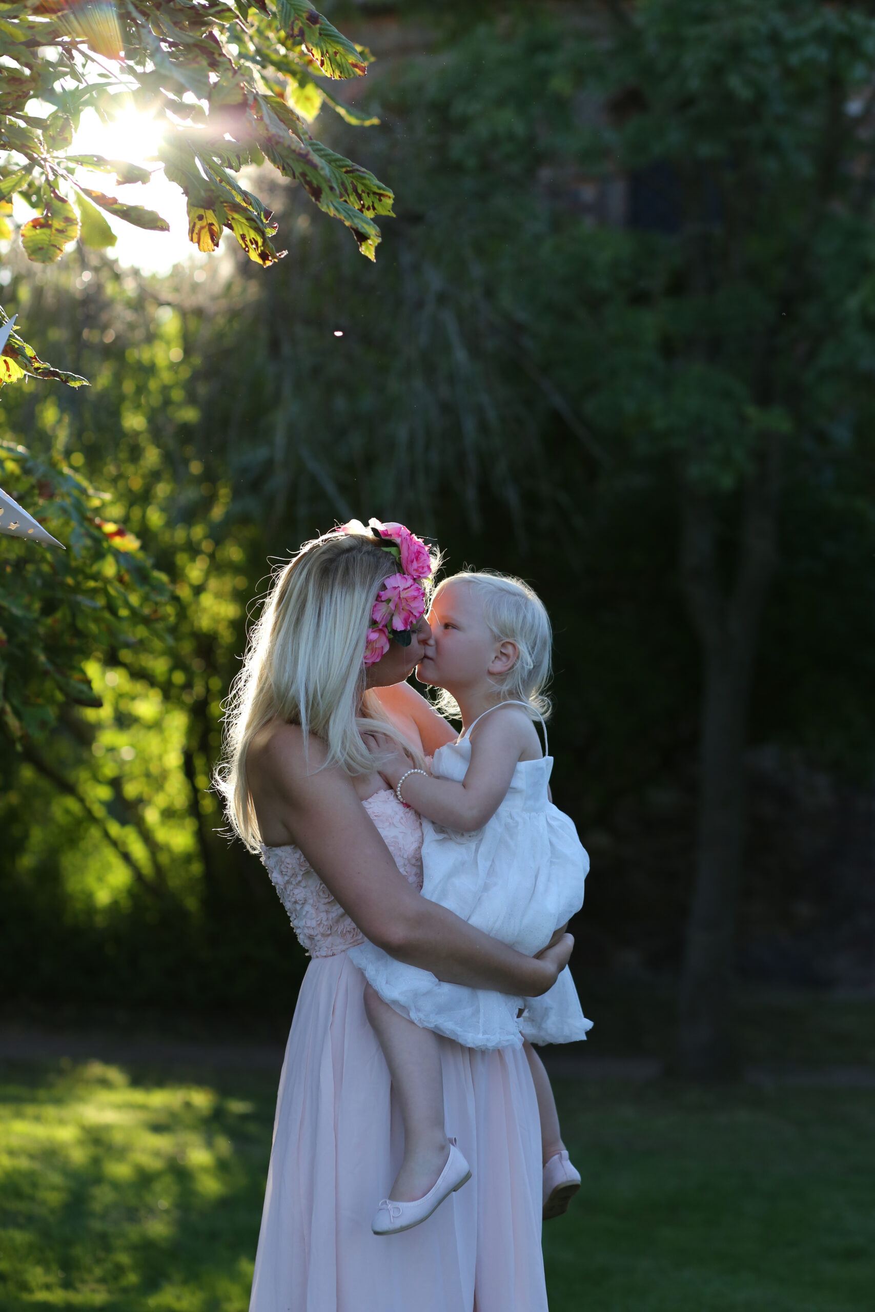 Eine Mama hält ihre kleine Tochter auf dem Arm und küsst sie zärtlich im herbstlichen Wald.